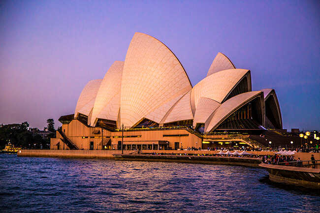 Sydney Opera House up close, amply lit by purple sky and waters below