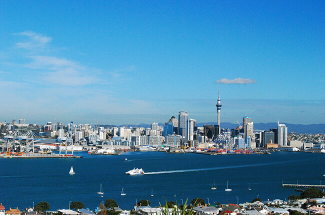 Bright photo of Auckland skyline at daytime, with boats sailing in the harbour