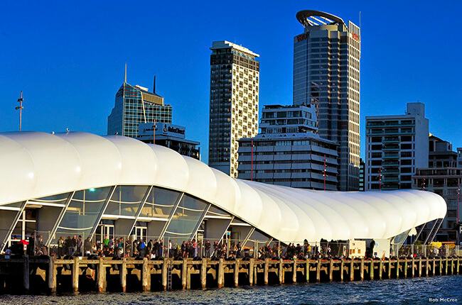 The wave-like architecture of the Queens Wharf in Auckland, with skyscrapers in the background